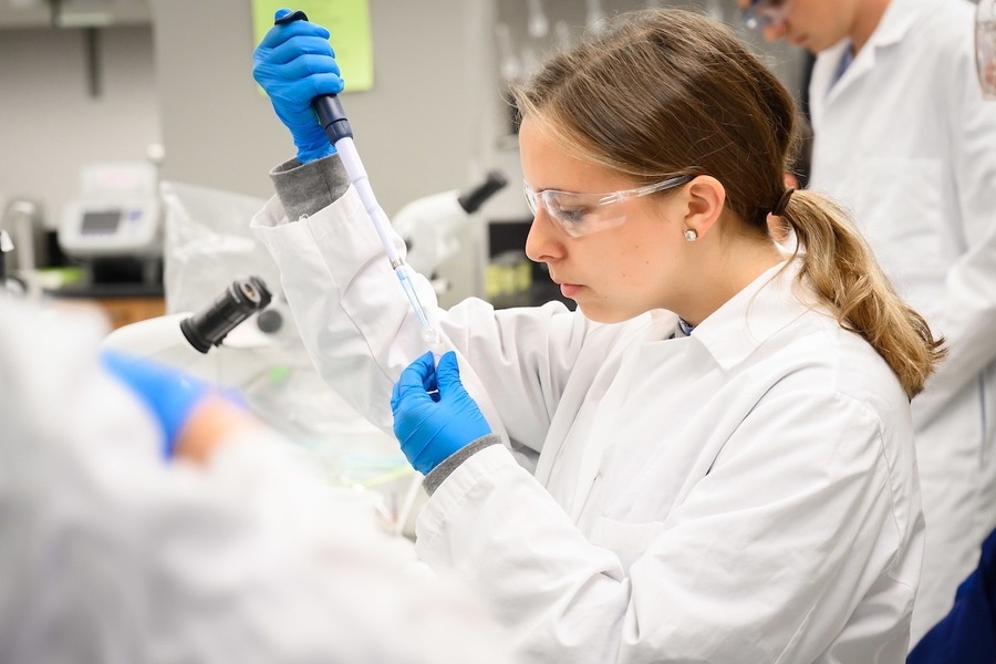 Undergraduate Lab student with syringe wearing white lab coat and goggles