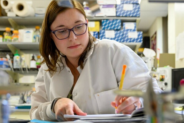 Student wearing lab coat jots notes in a lab