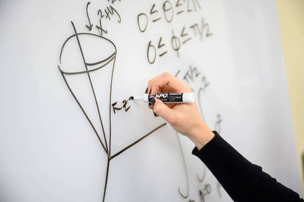 Hand writes math formula on whiteboard with black marker