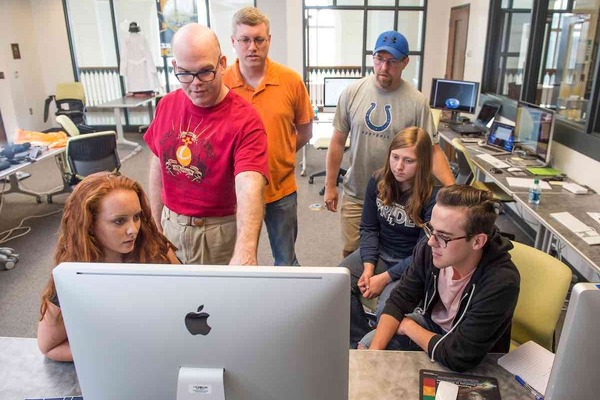 Students and instructor gather around computer