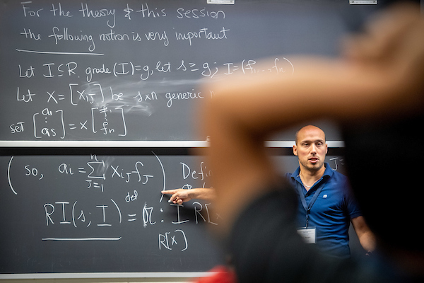 Teacher stands in front of a large blackboard covered in mathematic formulas and teaches