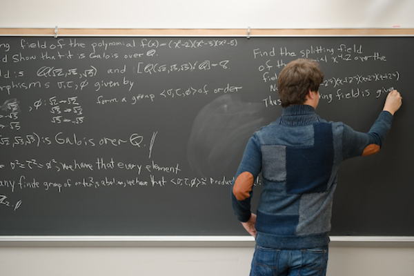 Student writes mathematics formulas at a chalkboard