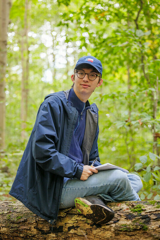 Ecology field trip: John Lesage sits perched on a log in the woods