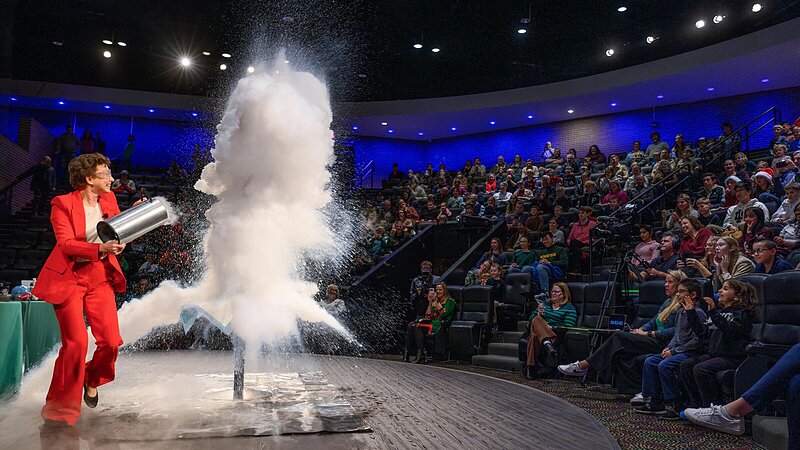 Dr. Tatiana pours hot water into liquid nitrogen, creating a large, white vapor cloud at the 2025 Christmas Lecture.