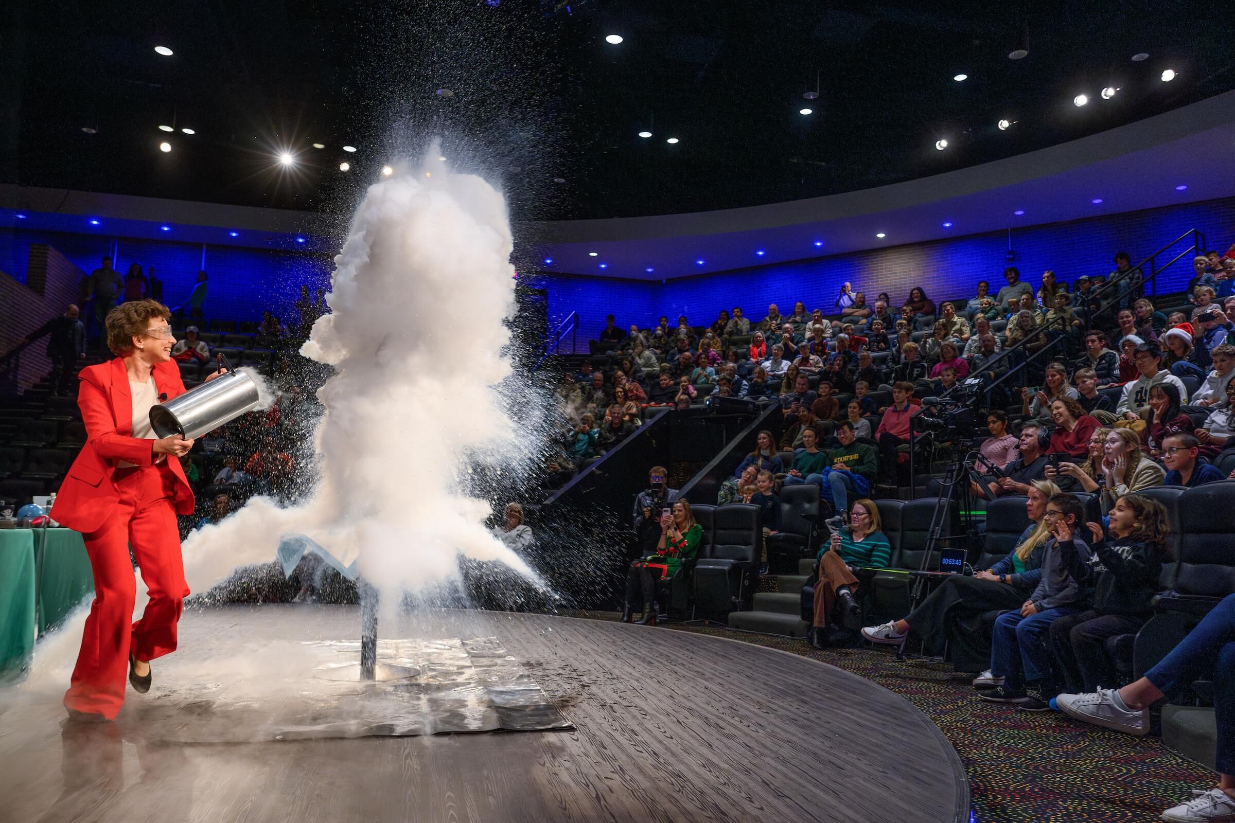 Dr. Tatiana pours hot water into liquid nitrogen, creating a large, white vapor cloud at the 2025 Christmas Lecture.