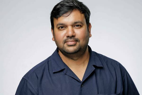 Pratik Yadav, with dark hair and a beard wearing a dark blue shirt looks at the camera with a pleasant expression.