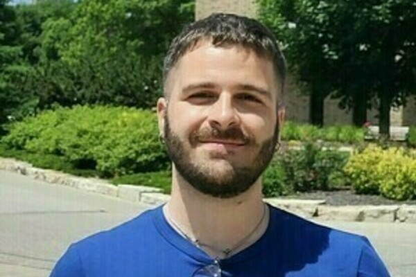 Assistant Professor Gioacchino Antonelli, with a beard and blue shirt smiles, with the Notre Dame Main Building's Golden Dome behind him.